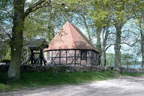 Un edificio de estilo Tudor tradicional con techo cónico, rodeado de árboles y un muro de piedra.