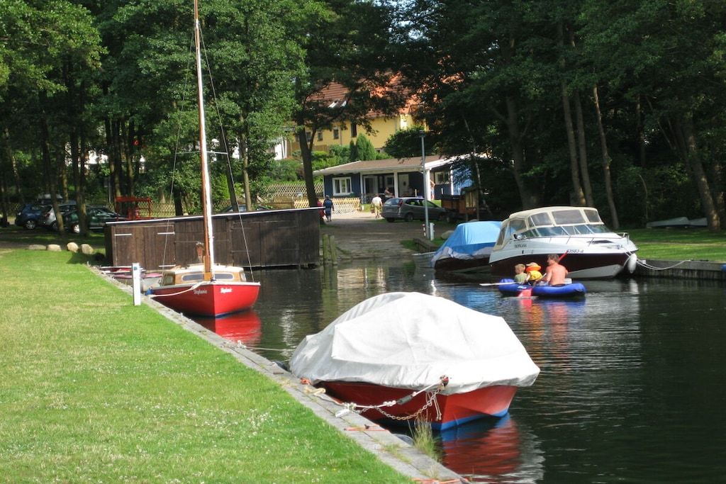 A calm waterway with boats docked, a grassy bank, and a building in the background.