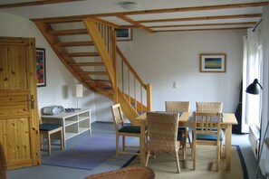 Ein Zimmer mit einer Holztreppe, einem Esstisch mit Stühlen, einem Radio und einem Bücherregal.