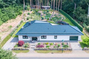 A modern two-story house with a sloped roof, surrounded by a well-maintained garden and a forested area. - Holiday home Molchow (Molchow)