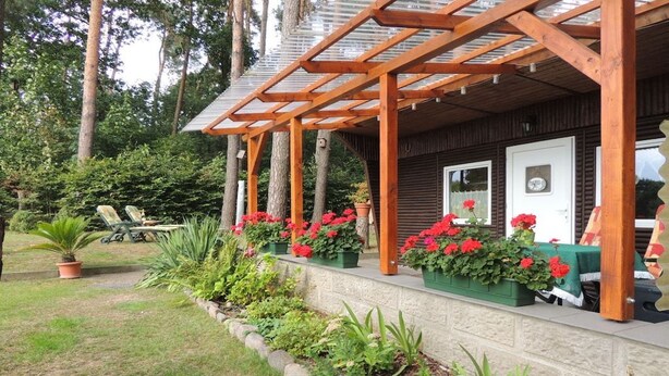 Un portico in legno con un'area salotto coperta, circondato da vasi di piante e fiori.