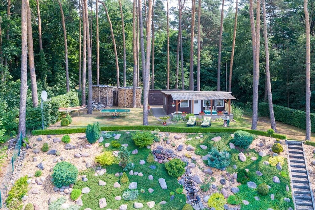 Une cabane entourée d’une forêt, avec un jardin bien entretenu et un chemin dégagé menant à l’entrée.