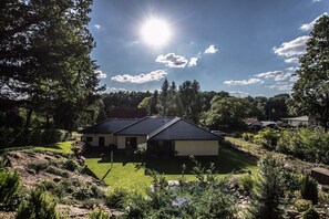 Une maison avec un toit en pente, entourée d’un jardin bien entretenu et d’arbres.