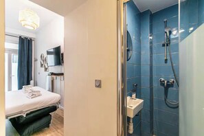 A hotel room with a bed, a TV, a shower with a handheld showerhead, and a sink. - Cosy Studio - 2P - Parmentier / Voltaire (Paris)