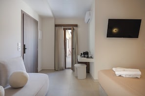 A hotel room with a sofa, a small table with a towel, a TV mounted on the wall, and a bathroom visible through a door. - Verano suites- Premium suite, Luxury suites in the center of Rethymno (Rethymno)