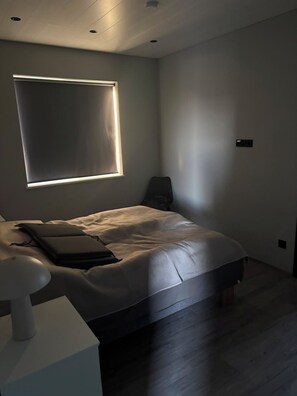 A modern bedroom with a bed, bedside table, and a window with blinds.