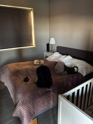 Hotellihuone, jossa on sänky, yöpöytä, lamppu ja vauvansänky.