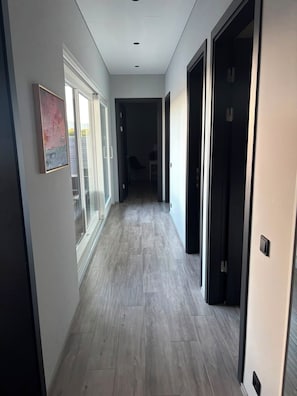A hallway with a light-colored floor, a framed picture on the left wall, and a door on the right.