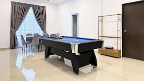 Una mesa de billar en una habitación con una puerta, una ventana con cortinas y una zona de estar con sillas.