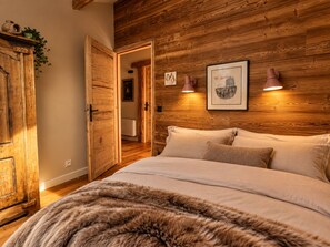 A bedroom with a wooden headboard, a bed with white bedding, a fur throw, and two wall-mounted lamps. - A natural paradise just 20 minutes from Vars—a magnificent chalet in the heart of the Ubaye Valley (Saint-Paul-sur-Ubaye)