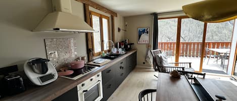 A modern kitchen with a large island, a dining area with a table and chairs, and a view of a wooden deck outside.