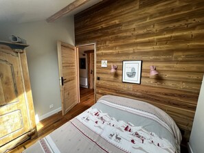 Een slaapkamer met een houten wand, een bed met een beddeken met patroon, een garderobe en een deur naar een andere kamer.