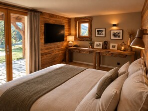 Een slaapkamer met een groot bed, een houten bureau, een televisie en een raam met uitzicht op bomen.
