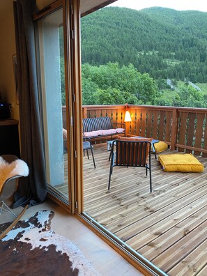 Een houten terras met buitenmeubilair, een bank en een lamp.