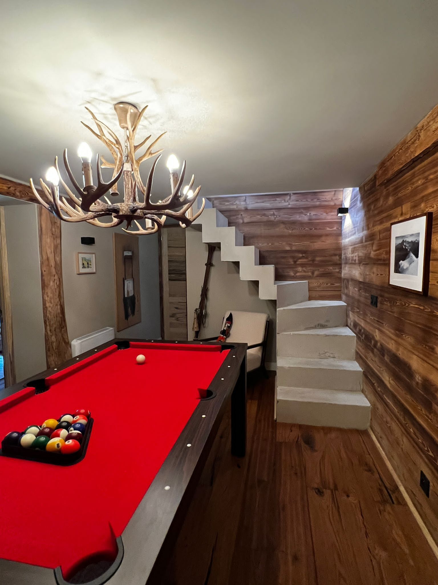 Une table de billard avec des billes, un lustre et un escalier.