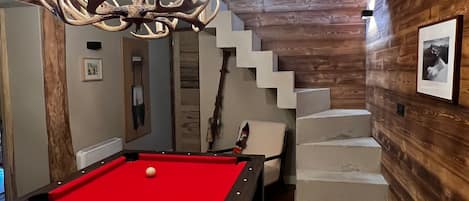 A pool table with balls, a chandelier, and a staircase.