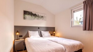 Cama doble con cabecera, mesitas de noche con lámparas, ventana con cortinas y una obra de arte colgada en la pared.
