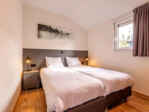 A double bed with a headboard, bedside tables with lamps, a window with curtains, and a wall-mounted artwork. - Riverside Family Lodge Stay for 6 (Kerkdriel)