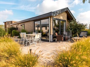 A modern house with a patio area featuring a table and chairs, surrounded by tall grasses. - Riverside Family Lodge Stay for 6 (Kerkdriel)
