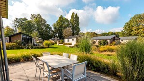 Un patio con mesa y sillas, rodeado de un jardín y vistas a casas.