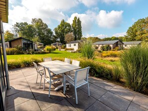 A patio with a table and chairs, surrounded by a garden and a view of houses. - Riverside Family Lodge Stay for 6 (Kerkdriel)