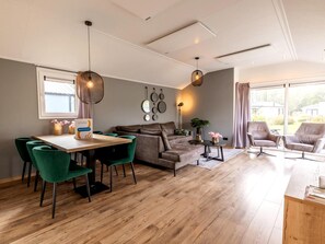 A modern living room with a dining area, a sofa, two armchairs, and a table with chairs. - Riverside Family Lodge Stay for 6 (Kerkdriel)