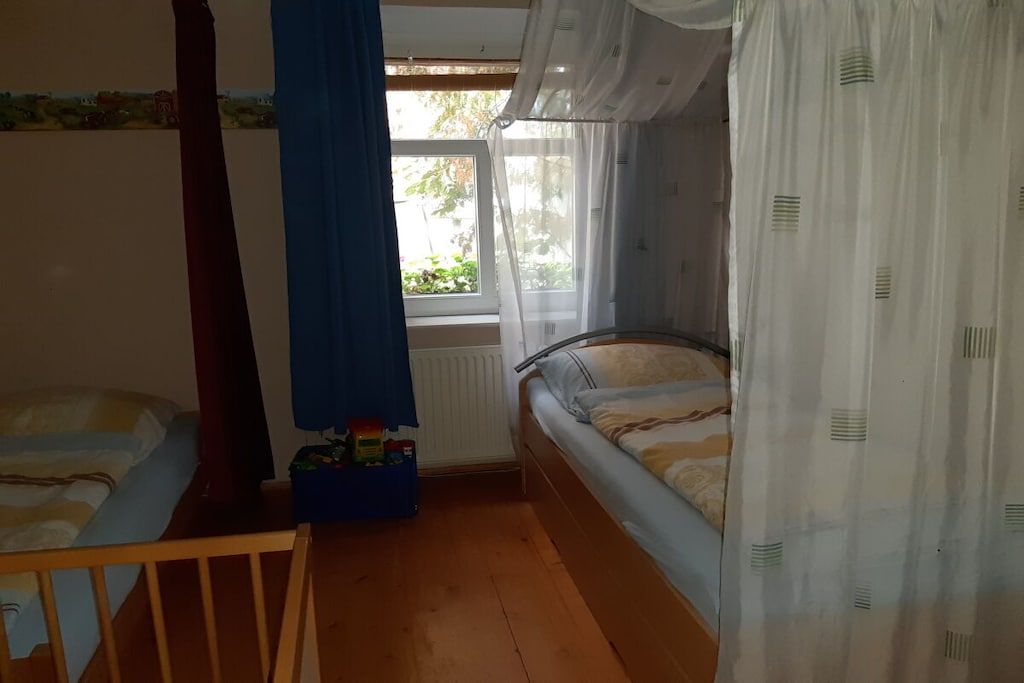 A bedroom with two beds, a window with curtains, a radiator, and a wooden floor.