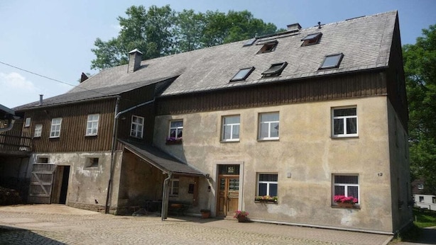 A two-story building with a sloped roof, multiple windows, and a visible entrance. - Farmhouse with 2 bedrooms (Elterlein OT Hermannsdorf)