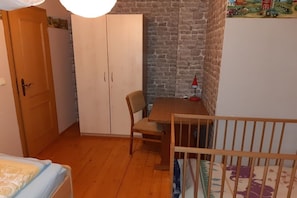 A room with a wooden floor, a bed with a patterned bedspread, a wooden wardrobe, a table with a chair, and a crib. - Farmhouse with 2 bedrooms (Elterlein OT Hermannsdorf)