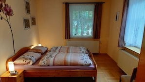 A bedroom with a wooden bed, a bedside table with a lamp, a window with curtains, and a radiator. - Farmhouse with 2 bedrooms (Elterlein OT Hermannsdorf)
