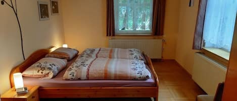 A bedroom with a wooden bed, a bedside table with a lamp, a window with curtains, and a radiator.