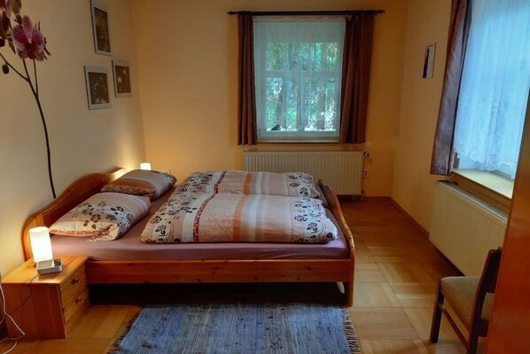 A bedroom with a wooden bed, a bedside table with a lamp, a window with curtains, and a radiator.