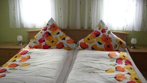 A double bed with floral bedding, two bedside tables with lamps, and a window with curtains. - Holiday home with 2 bedrooms (Reinhardtsdorf)