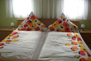 A double bed with floral bedding, two bedside tables with lamps, and a window with curtains. - Holiday home with 2 bedrooms (Reinhardtsdorf)