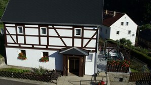 A traditional half-timbered building with a dark roof, a small entrance, and flower boxes on the ground floor. - Holiday home with 2 bedrooms (Reinhardtsdorf)