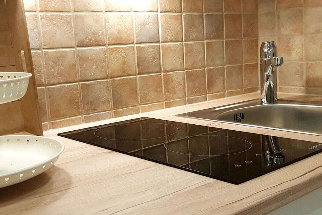 Cozinha com fogão por indução preto, pia de aço inoxidável e backsplash em tom claro.