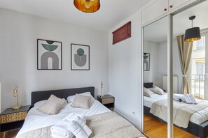 A modern bedroom with a large bed, bedside tables, a mirror, and abstract wall art. - Apartment Pantheon/saint Germain des Pres (Paris)