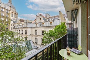 A balcony with a view of historic buildings, a table with a book and a glass of drink, and a railing. - Apartment Pantheon/saint Germain des Pres (Paris)