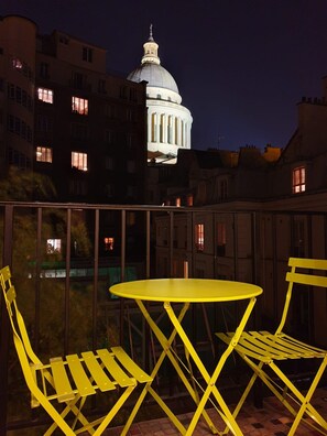 A balcony with yellow chairs and a table, overlooking a building with a dome and illuminated windows at night. - Apartment Pantheon/saint Germain des Pres (Paris)