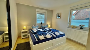 Ein Schlafzimmer mit einem Bett, Nachttischen, einem Fenster mit Jalousien, einer Heizung und einem Bild an der Wand.