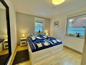 Een slaapkamer met een bed, nachtkastjes, een raam met zonwering, een radiator en een schilderij aan de muur.