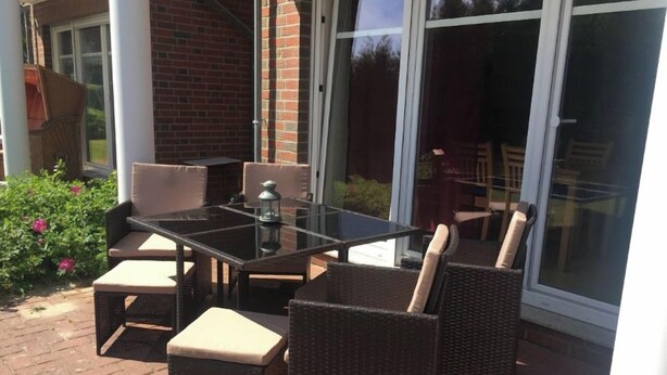 Eine Terrasse im Freien mit einem Glastisch und Korbstühlen.