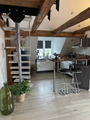 Une cuisine moderne avec un plafond en bois, un escalier en colimaçon en métal et un coin bar avec des tabourets.