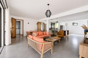 Een ruime woonkamer met een bank, salontafel en eettafel. Achtergrond is een keuken en een deur naar een andere kamer.