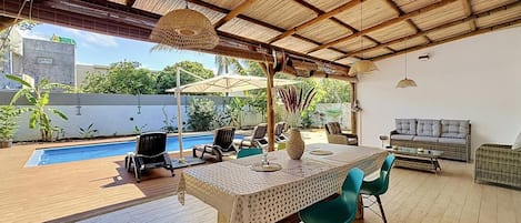 An outdoor patio with a pool, wooden deck, and a table with chairs.
