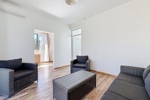 A spacious living area with wicker furniture, a wooden coffee table, and large windows allowing natural light. - 10 minutes from the public beach at GND GAUBE: a charming house with a pool (Grand Gaube)