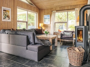 A cozy living room with a grey sofa, a wooden table, a small chair, and a fireplace. - 6 Person Holiday Home in Saeby (Sæby)