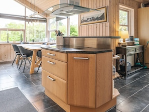 A kitchen with wooden cabinets, a countertop, and a window with a view of greenery. - 6 Person Holiday Home in Saeby (Sæby)