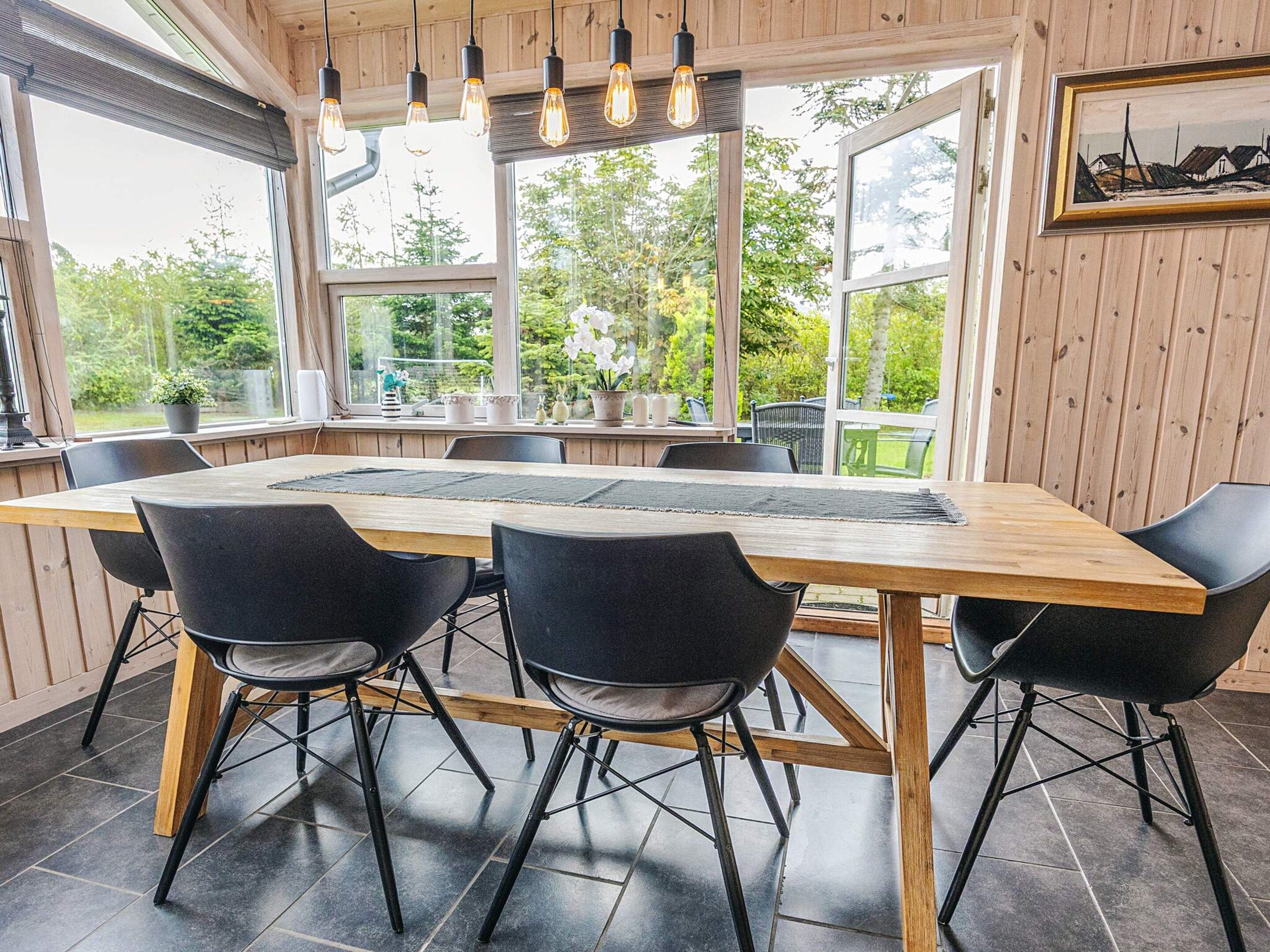 A dining area with a wooden table, black chairs, and a view of greenery outside.