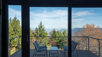 Une terrasse avec deux chaises et une table, offrant une vue sur une forêt et des montagnes.